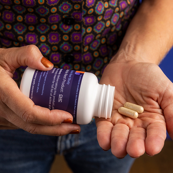 Left hand holding a sample Radicle Rest Product pill bottle, and pouring two pills to the right hand.